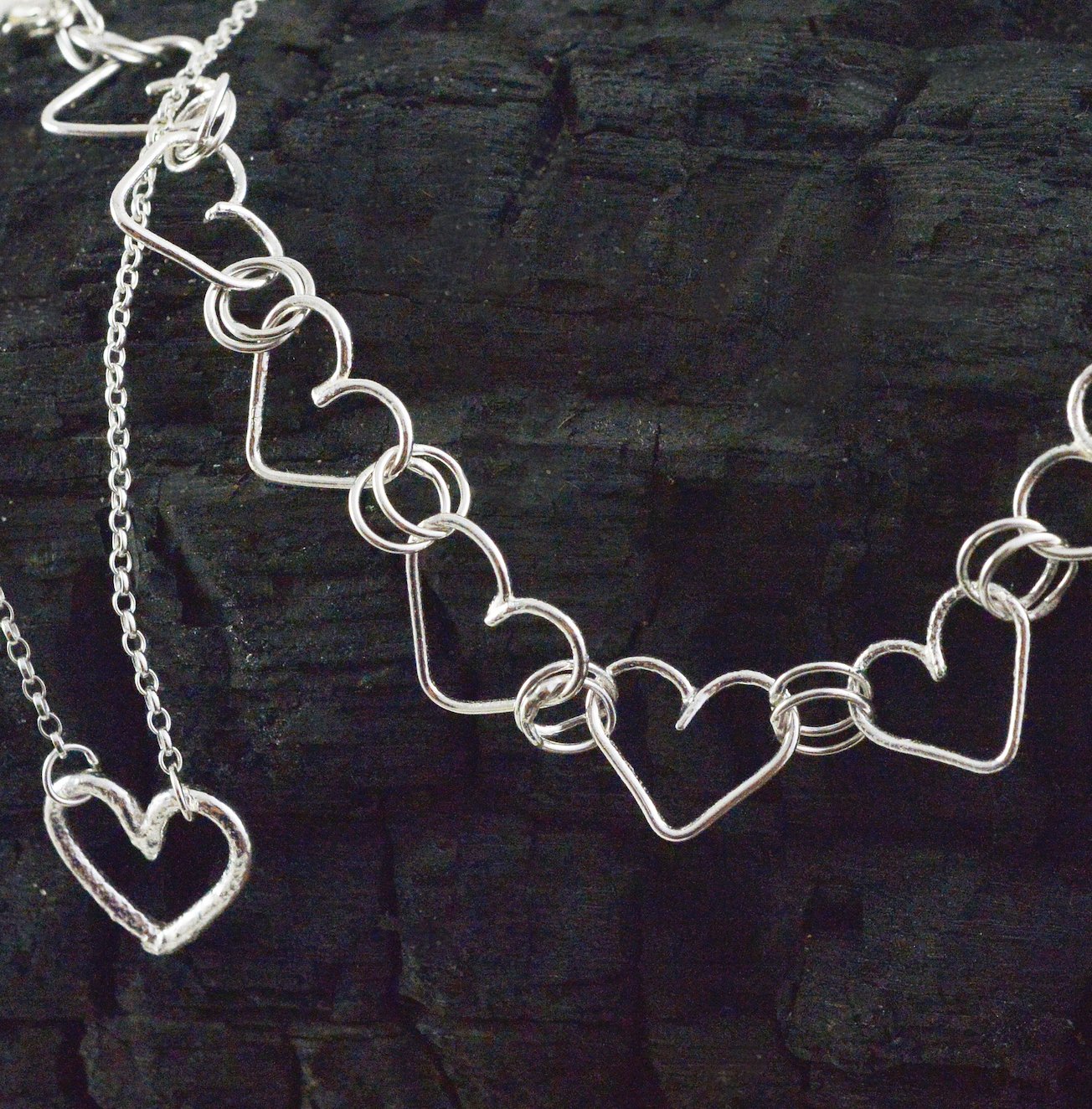 Heart necklace and bracelet on a charcoaled piece of wood